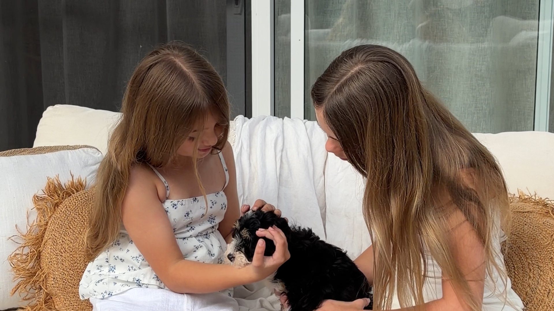 Two girls sitting on an outdoor couch with a Bernedoodle puppy