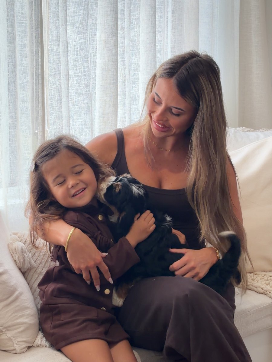 A woman and a young girl sitting on a couch holding a Bernedoodle puppy