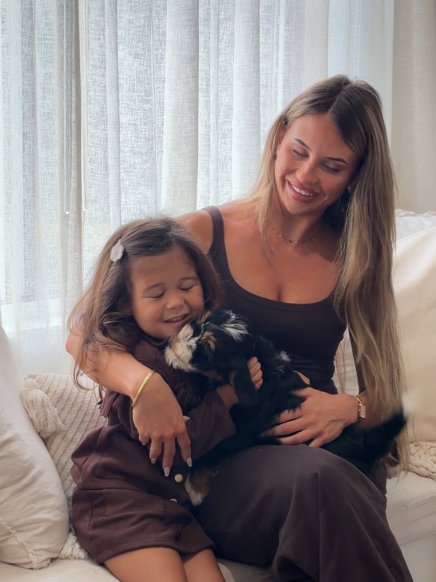 A mother and daughter holding a Bernedoodle puppy on a couch